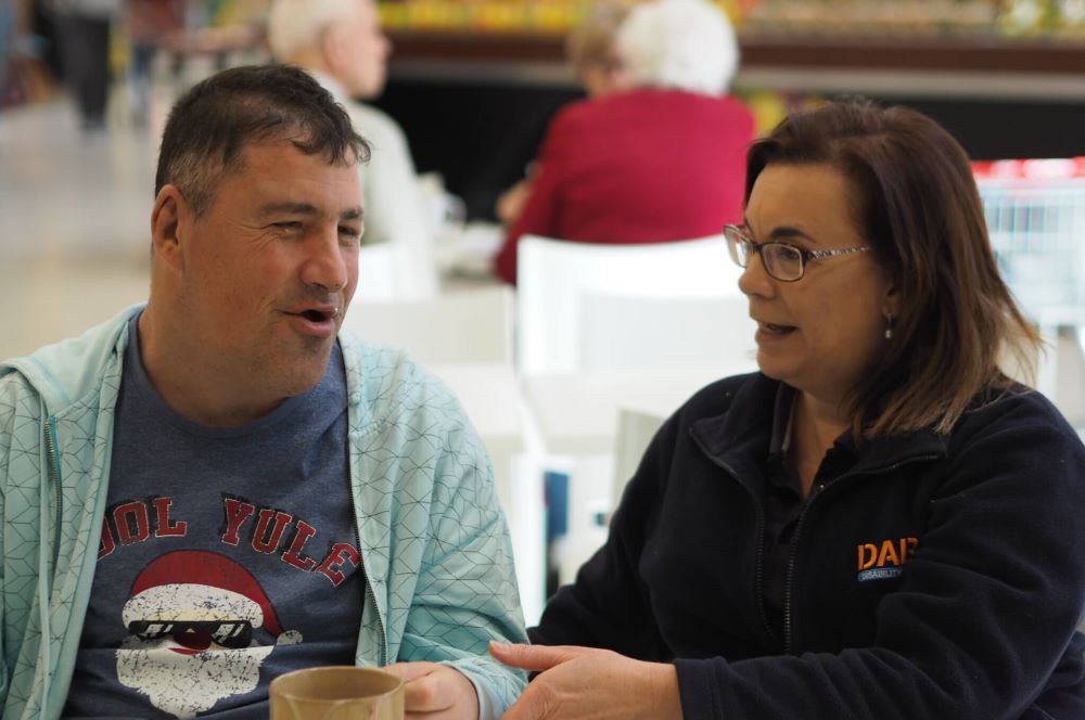 A support person and a person with a disability having a discussion over coffee